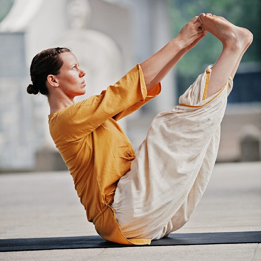 A woman performing an Angamardana yoga pose in front of a building.