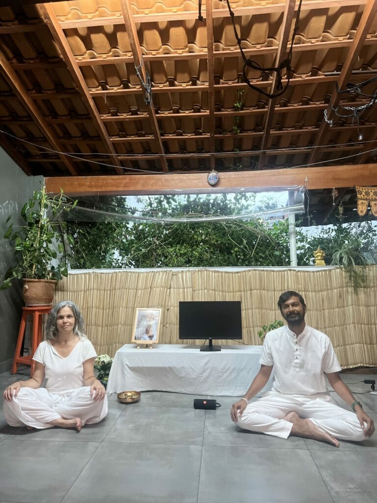A man and woman in white sitting on the floor and meditating.